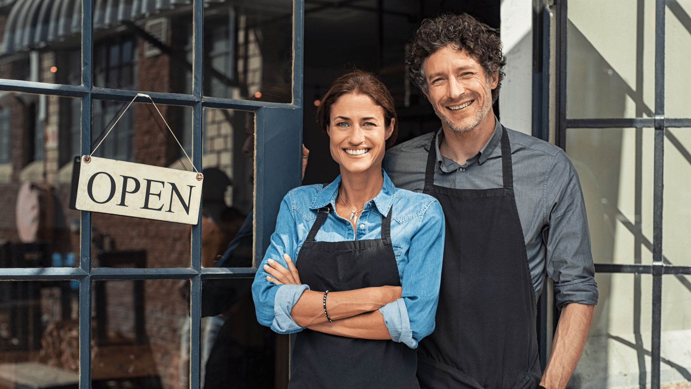 Small business owners standing in front of their shop with open sign, representing compliance with Beneficial Ownership Information (BOI) reporting requirements.